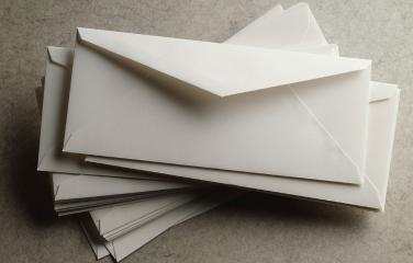 A stack of white envelopes sits on top of a grey marble table.