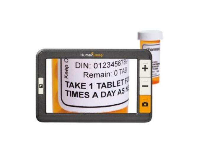 A handheld electronic magnifier enlarges a prescription bottle label, making the text readable.