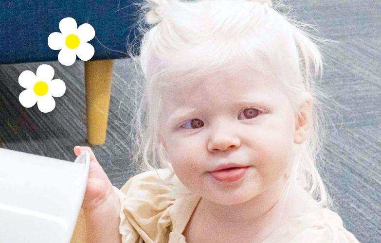 A little blonde girl in a yellow dress is looking into the camera.